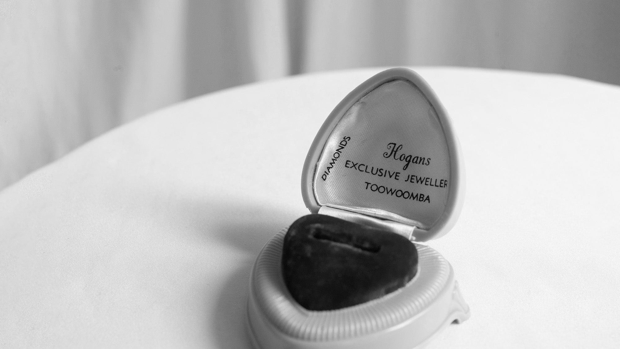 Black and white photograph of vintage heart shaped ring box with open lid.