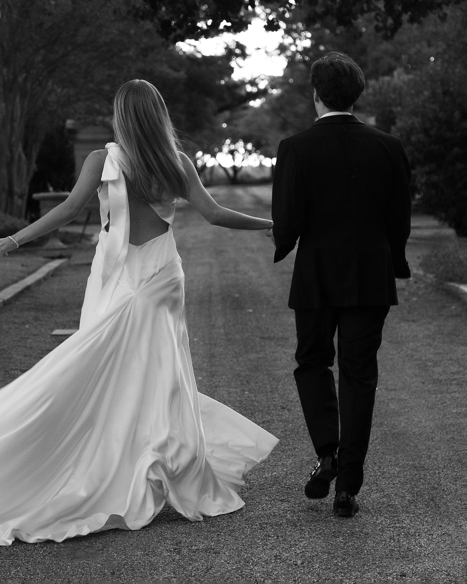 Black and white photograph of bride and groom holding hands and running away from camera.