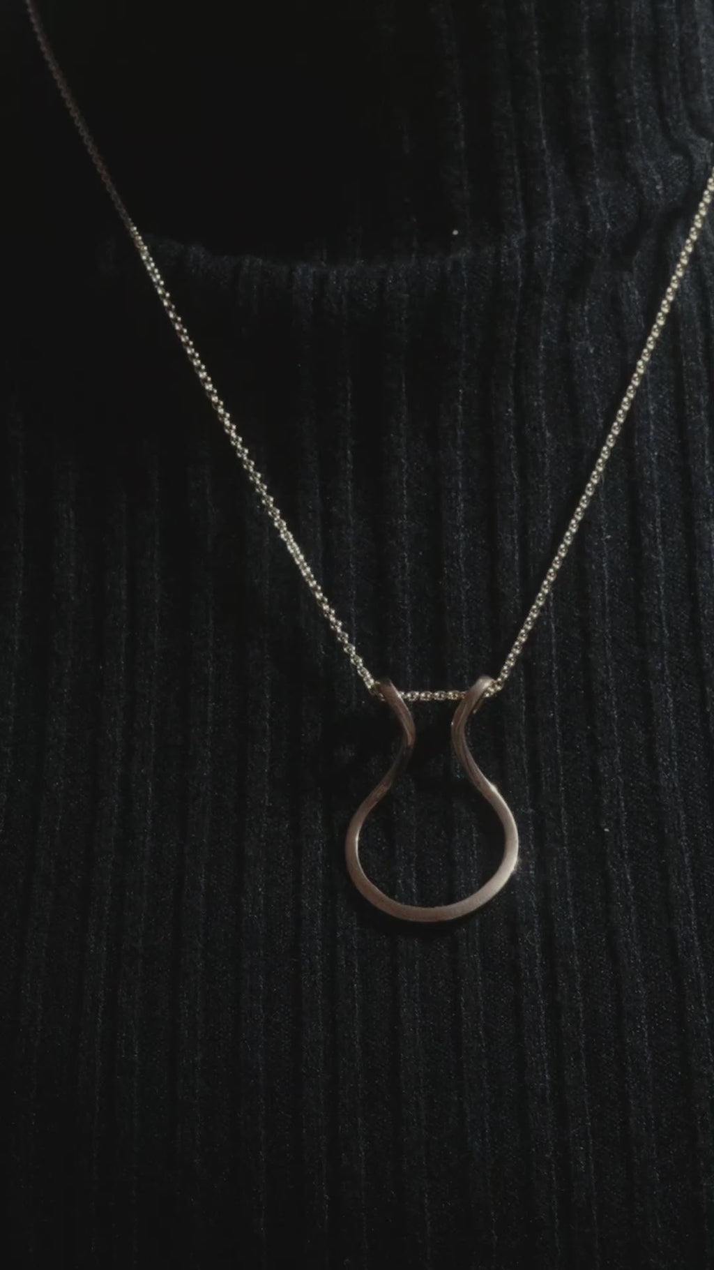 Model wearing black turtleneck, demonstrating how to thread a ring onto a ring keeper pendant.