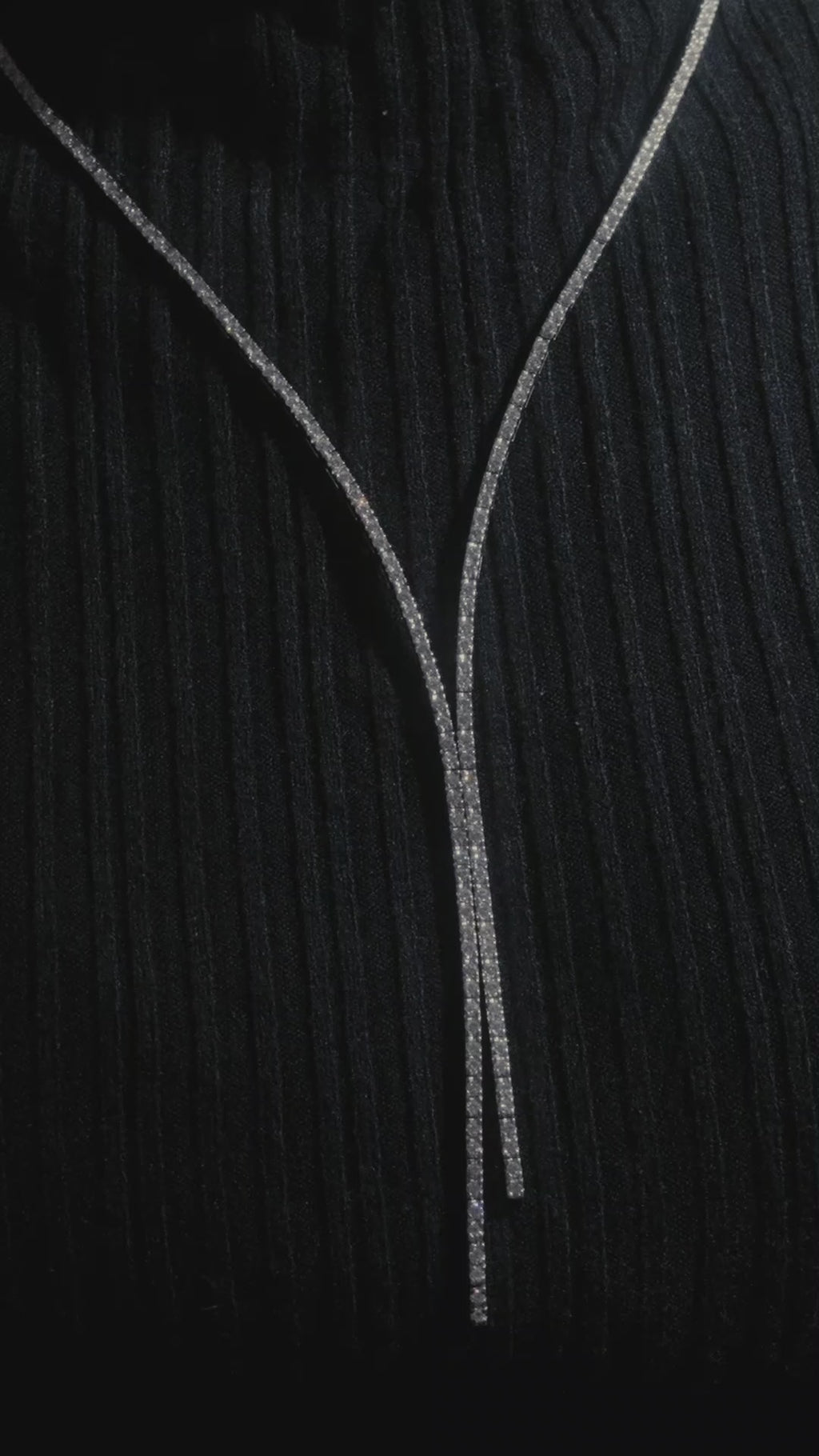 Close up of white gold split style diamond set drop necklace on model wearing a black turtleneck.